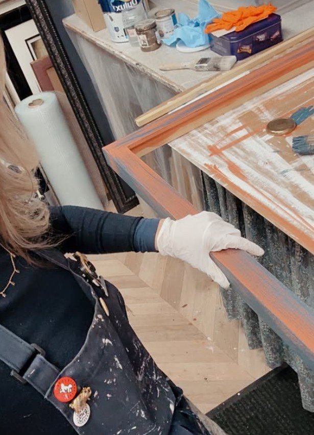 Hand finishing a distressed gold picture frame at the workbench